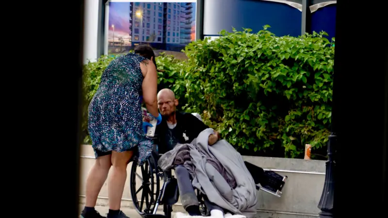 Karen, una trabajadora de rehabilitación, atiende a un hombre de aspecto demacrado en silla de ruedas en una zona exclusiva de la ciudad.